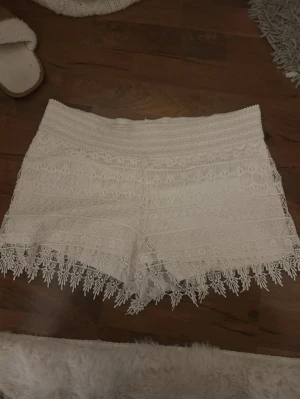 Vita spetsshorts - Säljer ett par vita shorts med vacker spets och broderade detaljer. De har en bred resår i midjan och fina fransar längs bensluten. Perfekta för sommaren. Köpte på vinted och lappen borta så vet ej märke, säljaren inann påstod storlek S/M och det stämmer nog bra. Jättelite nopprar på baksidan, se sista bilden
