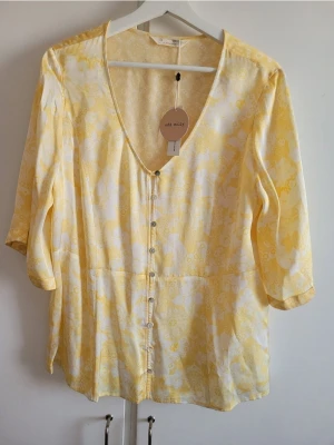 Gul blommig blus Odd Molly - Söt gul blus från Odd Molly med blommigt mönster och knappar framtill. Blusen har djup V-ringning och trekvartsärm. Tillverkad i ett lätt och mjukt  viskos tyg som ger en luftig känsla. Perfekt för dig som gillar ljusa och somriga plagg.