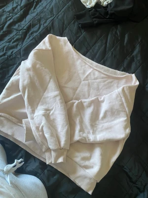 Ljusrosa hoodie med bred hals - Säljer en ljusrosa hoodie med bred, öppen halsringning och ribbade muddar vid ärmslut och nederkant. Tröjan är tillverkad i mjukt bomullsmaterial och har en avslappnad passform som är perfekt för chill dagar.