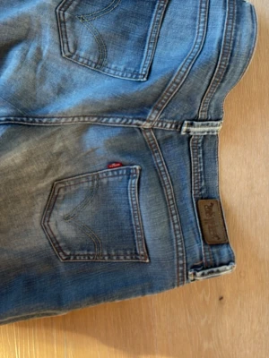 Blå Levi's jeans med slitningar - Säljer mina feta vintage blå Levi's jeans med snygga slitningar och tvättad look. Femficksmodell med Levi's ikoniska röda etikett på bakfickan och läderpatch i midjan. Flared passform, storlek 30/30. Skriv för frågor🙏