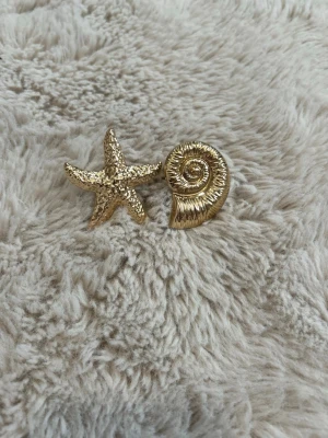 Guldiga ringar med sjöstjärna & snäcka - Ringar i form av en sjöstjärna och en snäcka i guldig metall. Snyggt strandinspirerat motiv som verkligen sticker ut. Jag har bara provat dem på, alltså så är dem inte använda. Man kan även justera storleken på ringarna 