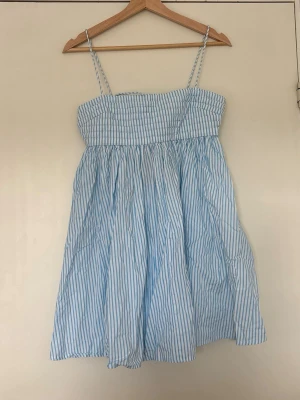 Blåvit randig sommarklänning ASOS - Söt blåvit kortklänning från ASOS DESIGN med tunna axelband och smockad rygg. Klänningen har ett luftigt fall 