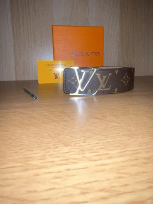 Snygg brunt skärp med monogram - Säljer ett brunt skärp med klassiskt monogrammönster och en stor -spänne i gulda Skärpet är tillverkat i skinn och har exklusiv känsla. Perfekt för dig som vill ha en ikonisk accessoar med lyxig design.