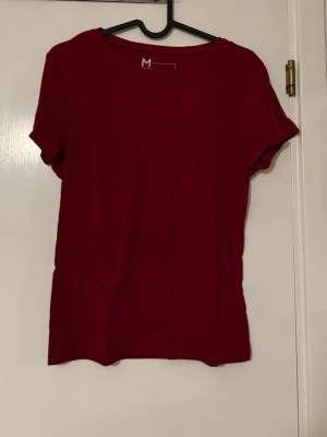 Mörkröd basic t-shirt i bomull - En enkel och stilren mörkröd t-shirt i mjuk bomull. T-shirten har rund halsringning och korta ärmar, perfekt för en avslappnad look. Passformen är normal och materialet känns skönt mot huden.