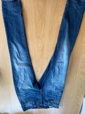 Blå slim fit jeans med slitningar - Snygga blå slim fit jeans med lätt slitna detaljer och tvättade partier för en cool look. Klassisk femficksmodell med dragkedja och knapp. Perfekta till sneakers och hoodie för en avslappnad stil.
