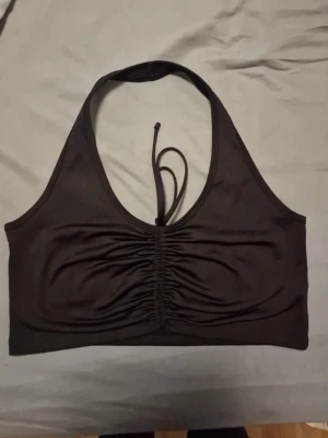 Svart  halterneck topp med snörning - Snygg svart halterneck topp med snörning framtill och rynkade detaljer över bysten. Toppen har en croppad passform och knyts i nacken. Perfekt för dig som gillar en enkel men trendig look.