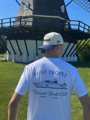 Voronado Yacht Club T-shirt - Vit t-shirt från Voronado Yacht Club med tryck på ryggen av en yacht, texten 'Saint Tropez' och fransk flagga. Framtill står det 'Voronado Yacht Club' i liten text. Klassisk passform och rund hals, perfekt för sommardagar.