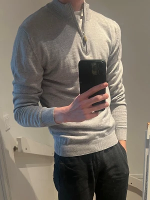 Ljusgrå halvzip-tröja Stenströms - Snygg ljusgrå tröja med halv dragkedja och ribbade muddar. Tröjan har en hög krage och är tillverkad i mjuk merinoull, perfekt för lager-på-lager. Enkel och stilren design som passar till det mesta.