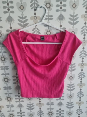 Rosa ribbad croppad topp Gina Tricot - Snygg rosa croppad topp från Gina Tricot med ribbad struktur. Toppen har korta ärmar och en djup rundad halsringning. Perfekt att styla med höga jeans eller kjol för en trendig look.
