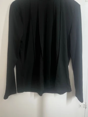 Svart långärmad polotopp - En stilren svart polotopp med lång ärm och detaljer framfill. Toppen har en klassisk polokrage och är tillverkad i ett mjukt och stretchigt material som sitter snyggt på kroppen. Perfekt att matcha med jeans eller kjol för en clean look. (Finns i vit också) 