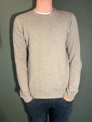 Ljusgrå basic tröja i bomull - En enkel och stilren ljusgrå tröja med rund hals och långa ärmar. Tröjan har ribbade muddar vid ärmslut och nederkant, perfekt för en clean och avslappnad look. Tillverkad i mjuk bomull som känns skön mot huden. Nypris ca 899