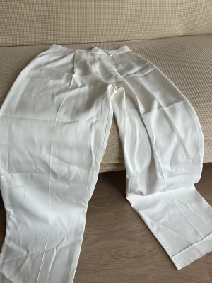 Vita vida linnebyxor - Snygga vita linnebyxor med rak och vid passform. Byxorna har hög midja och klassisk look, perfekta för en avslappnad och trendig stil. Tillverkade i lätt och luftigt linnematerial som passar perfekt till sommaren.