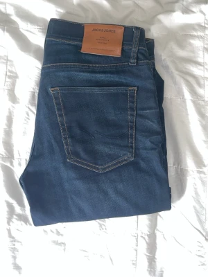 Mörkblå jeans från Jack & Jones - Snygga mörkblå jeans från Jack & Jones med klassisk femficksdesign och kontrastsömmar. Jeansen har en rak passform och är tillverkade i ett mjukt denimtyg med läderpatch bak i midjan.