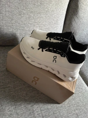 On cloud - Stilrena sneakers från On cloud i vitt med svarta detaljer och svart plös. Storlek 42. Ny pris ligger runt 2100kr
