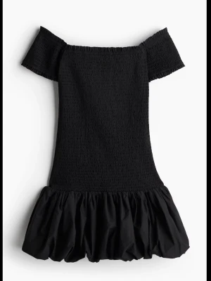 Svart offshoulder kortklänning - Trendig svart kortklänning med offshoulder och smockad överdel. Kjolen har volang och ballongformad nederkant som ger en cool och lekfull vibe. Perfekt för dig som vill sticka ut med en stilren look.