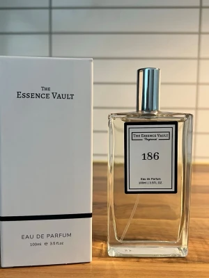 The Essence Vault 186 Eau de Parfum - Fräsch och stilren parfym från The Essence Vault, nummer 186. Kommer i en genomskinlig, fyrkantig glasflaska med silverfärgad kork och svartvit etikett. Förpackningen är vit med minimalistisk design. Innehåller 100 ml Eau de Parfum.