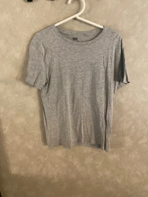 Grå basic t-shirt från 157 - Enkel och stilren grå t-shirt från 157 i mjuk bomullsblandning. T-shirten har rund halsringning och korta ärmar, perfekt för en avslappnad look. Materialet består av 90% bomull och 10% viskos.