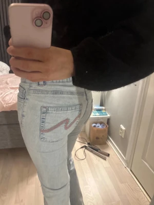 Ljusblå bootcut jeans - Säljer ett par ljusblå bootcut jeans med snygg rosa brodyr på bakfickan. 
