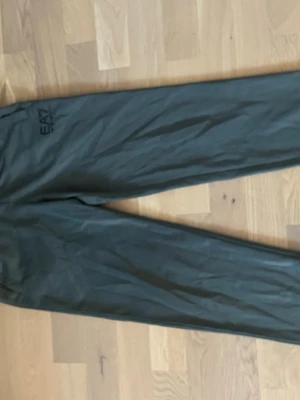 EA7 byxor - Säljer ett par mörkgröna mjukisbyxor från EA7 Emporio Armani. Byxorna har en avslappnad passform och är tillverkade i mjukt material som passar perfekt för chill dagar. EA7-loggan syns diskret på benet. Perfekta för en casual och sportig stil.