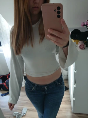 Vit långärmad crop top med knyt - Trendig vit långärmad crop top med vida ärmar och snygg knytning i ryggen. Toppen har en tight passform och är gjord i ett mjukt, stretchigt material som sitter skönt på kroppen. Perfekt för dig som vill ha en enkel men ändå unik topp till din outfit.