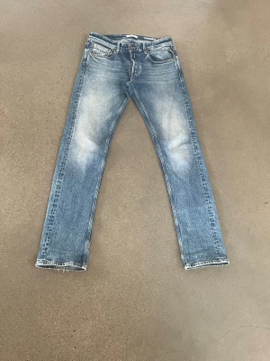 Blå raka jeans med slitningar - Ett par klassiska blå jeans med raka ben och snygga slitningar på både fram- och baksida. Jeansen har fem fickor och ljusare partier på låren för en cool, avslappnad look. Perfekta för dig som gillar en tidlös stil.