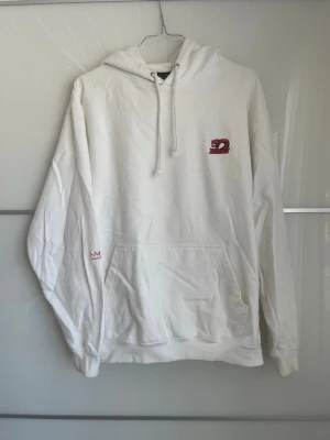 Vit hoodie från Hovr med ormtryck - Säljer en vit hoodie från Hovr med ett litet tryck av en röd orm och texten 'HOVAH' på bröstet. Hoodien har huva med dragsko, stor magficka och en liten krona broderad på ärmen. Perfekt för dig som gillar streetwear och enkel stil.