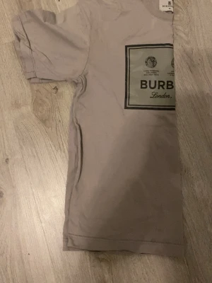 Beige Burberry t-shirt med tryck - Säljer en beige t-shirt från Burberry med klassiskt tryck på bröstet där det står 'Burberry London'. T-shirten har rund hals och korta ärmar. Perfekt för dig som gillar stilrena och exklusiva plagg.