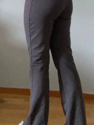 Mörkgråa bootcut kostym byxor - Säljer ett par mörkbruna bootcut byxor med hög midja och två knappar framtill. Byxorna har en smickrande passform och lätt utsvängda ben. Perfekta för dig som vill ha en trendig och bekväm look.