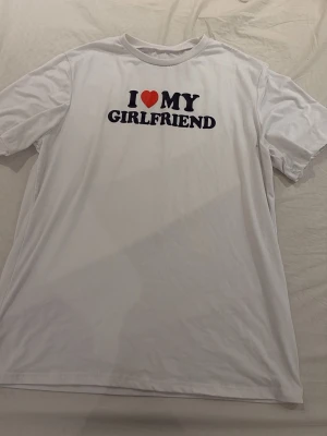 Vit t-shirt med I ❤️ MY GIRLFRIEND-tryck - Säljer en vit t-shirt med det ikoniska trycket 'I ❤️ MY GIRLFRIEND' i svart och rött på bröstet. Klassisk passform och rund halsringning. Perfekt för dig som vill visa lite extra kärlek i vardagen.