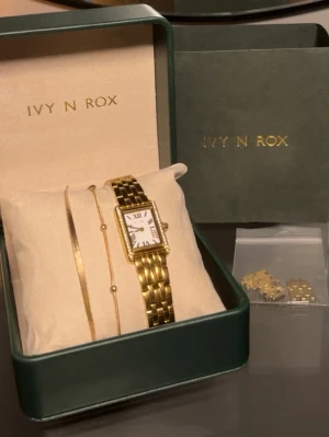 Guldfärgad klocka från Ivy N Rox - Stilren guldfärgad klocka från Ivy N Rox med rektangulär vit urtavla och romerska siffror. Klockan har en klassisk metallänk och levereras i originalask tillsammans med matchande armband och extra länkar. skicka gärna frågor eller prisförslag. Klockan är som ny 