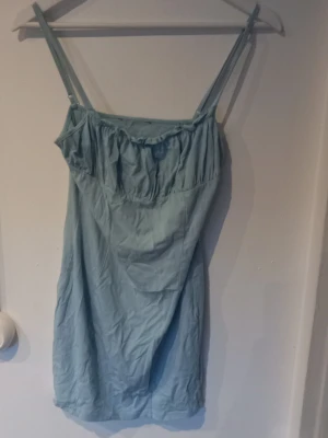 Ljusblått klänninh med smala axelband - Säljer ett ljusblått klänning med smala axelband och lätt rynkad detalj vid bysten. Klänning är i mjukt och tunt material, perfekt för varma nätter. Enkel och stilren design utan mönster.