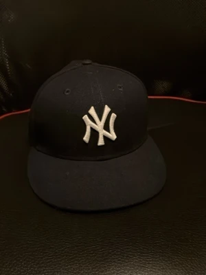 New era keps  - Klassisk svart keps från New Era med New York Yankees-logga broderad i vitt framtill. Kepsen har rak skärm och broderade ventilationshål. Perfekt för dig som gillar sportig och streetinspirerad stil. storlek 7 och tre åttondelar 