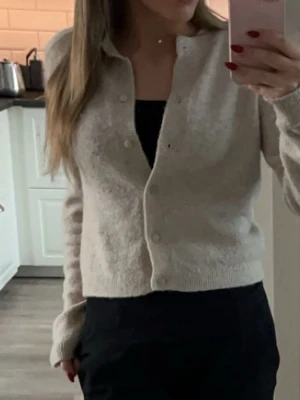 Beige kofta från Divided - Mysig beige kofta från Divided med rund halsringning och knäppning framtill. Koftan är ribbstickad vid ärmslut och nederkant, har en enkel och stilren design som passar perfekt till lager-på-lager. Tillverkad i mjukt material för extra komfort.