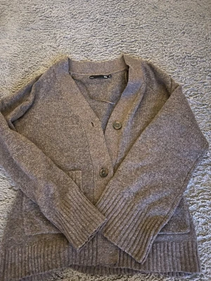 Brun stickad kofta med knappar - Mysig brun stickad kofta från lager med tre stora knappar framtill och djupa fickor. Koftan har ribbade muddar vid ärmslut och nederkant samt en avslappnad passform. Perfekt för lager på lager och chill dagar.