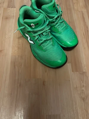 Newbalance hesilow - Säljer ett par gröna basketskor från New Balance med vit logga på sidan. Skorna har snörning, meshmaterial för bra ventilation och en högre modell som ger stöd runt ankeln. Perfekta för dig som vill sticka ut på planen med stilrena och sportiga skor.