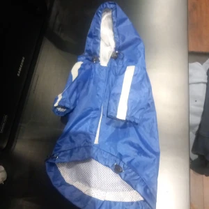 Blå regnjacka för hund med huva - Säljer en blå regnjacka för lite större en liten hund med vit reflexrand och huva. Jackan har öppning för sele eller koppel och är tillverkad i lätt, vattenavvisande material med meshfoder på insidan. Perfekt för promenader i regnet.