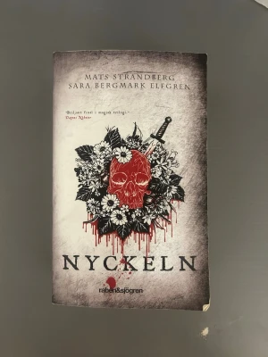 Bokserie av Strandberg/Elfgren - Tre böcker ur Engelsforstrilogin: 'Nyckeln', ’Cirkeln’ och 'Eld' av Mats Strandberg och Sara Bergmark Elfgren. Omslagen är svartvita med röda detaljer, illustrationer av dödskalle och hjärta bland blommor, tryckta i mjukt omslag. Perfekt för dig som gillar urban fantasy och spänning.