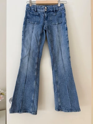 Blå bootcut jeans med framfickor - Säljer ett par blå bootcut jeans med markerade sömmar och stora framfickor. Jeansen har klassisk knappstängning och två bakfickor.