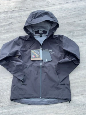 Arc'teryx jacka  - Snygg svart regnjacka från Arc'teryx med huva och vattentätt Gore-Tex-material. Jackan har hel dragkedja framtill, två dragkedjorförsedda fickor och justerbar huva. Perfekt för regniga dagar och outdoor-äventyr —>helt vattentät. Kvittot är bortslarvat, men bild finns, skickas dock endast vid köp (folk screenshotar). Storlek s, lite liten i storleken. Ställ frågor för mer!!
