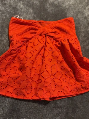 Röd  broderad tubtopp med spets - Snygg röd tubtopp med broderade blommor och spetsdetaljer. Toppen är ärmlös och har en smockad överdel som ger en bekväm passform. Perfekt för sommaren och ger en färgstark vibe till din outfit.