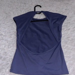 Mörkblå ärmlös topp med öppen rygg - Snygg mörkblå topp med ärmlös design och stor öppen rygg. Perfekt för dig som vill ha en trendig och stilren look. Toppen har en enkel rund halsringning och är gjord i ett mjukt, stretchigt material som sitter bekvämt.
