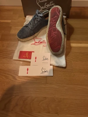 LjusblåaChristian Louboutin sneakers - Snygga gråa sneakers från Christian Louboutin i mocka med klassisk röd sula och vita kanter. Skorna har rund tå, matchande grå skosnören och diskreta sömdetaljer. Perfekta för dig som vill ha något exklusivt och stilrent. Skorna är väldigt fina dock ganska smutsiga men det är bara att tvätta bort så blir som som nya. Storlek: 43