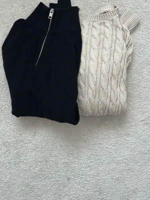 Svart ziptröja & beige kabelstickad tröja - Två stickade tröjor: en svart med hög krage och dragkedja framtill, samt en beige kabelstickad tröja med klassiskt flätmönster. Båda har lång ärm och ribbade detaljer. Perfekta för lager på lager och snygga till jeans eller kjol. Ena XL men liten i storlek så passar L och den andra M säljer båda för 300kr tillsammans.