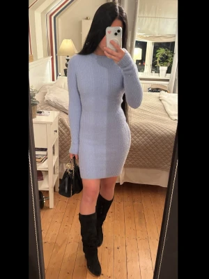 Ljusblå ribbad stickad klänning - Säljer en ljusblå stickad klänning med ribbad struktur och långärmad design. Klänningen är kort och har en rund halsringning, perfekt för att skapa en snygg och bekväm look. Fungerar lika bra hemma som borta. Passformen är tight och materialet är mjukt och stretchigt.