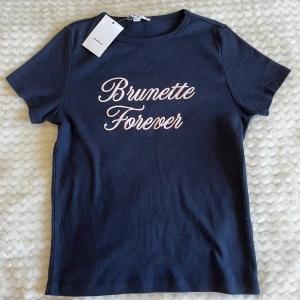 Mörkblå t-shirt Brunette Forever från Subdued - Mörkblå t-shirt från subdued med texten 'Brunette Forever' i ljusrosa. Den är i modellen baby tee. Väldigt mjuk och stretchig. Helt nytt skick med lappen kvar