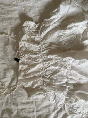 Vit linnetopp med knyt - Säljer en söt vit linnetopp med knytband på axlarna och rynkade detaljer. Toppen har en luftig och somrig känsla, perfekt till höga jeans eller kjol. Materialet känns lätt och andas, vilket gör den skön under varma dagar.