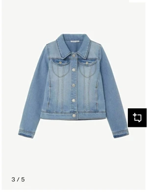 Jättesnygg ljusblå jeansjacka -  Ljusblå jeansjacka från Name It med klassisk krage, bröstfickor med knappar och markerade sömmar. Jackan har långa ärmar och stängs med metallknappar framtill. Endast använd några få gånger.