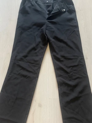 Svarta vida kostymbyxor - Säljer ett par svarta kostymbyxor från madlady med raka, vida ben med fickor bak 