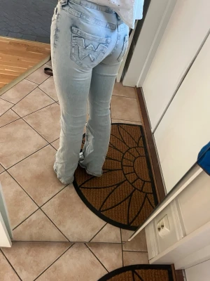 Ljusblå bootcut jeans från gina - Säljer ett par ljusblå bootcut jeans från gina med klassiska bakfickor och broderad W-logga. Jeansen har låg midja och är tillverkade i mjuk denim med lite stretch. Perfekta för en avslappnad och trendig look.