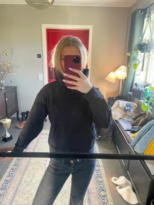 Svart hoodie med huva - Säljer en klassisk svart hoodie med huva och känguruficka framtill. Hoodien har en avslappnad passform och ribbade muddar vid ärmar och nederkant. Perfekt för en chill och enkel stil. Materialet känns mjukt och bekvämt.